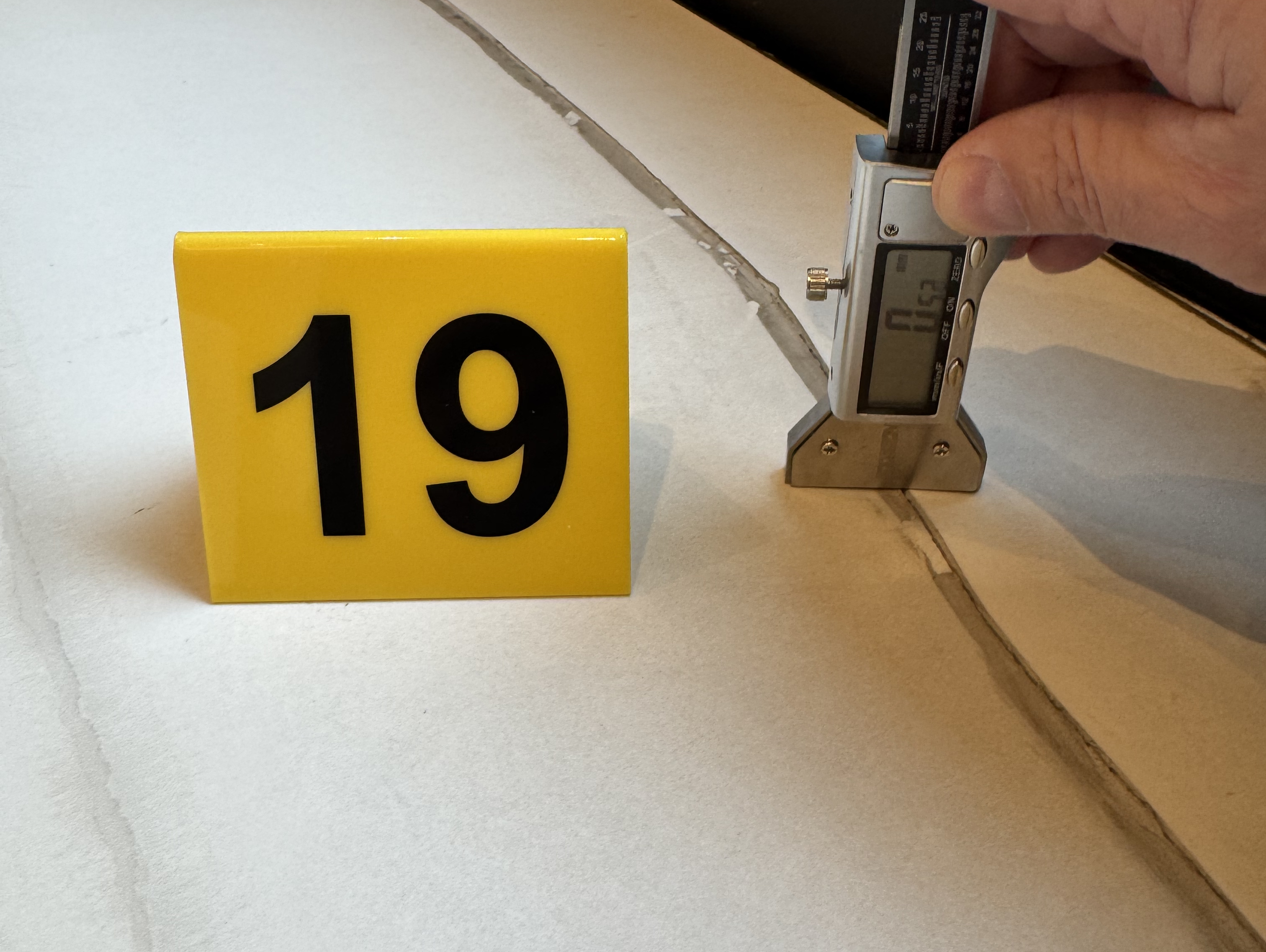 Digital caliper measuring crack width in stone tile floor with forensic evidence marker number 19