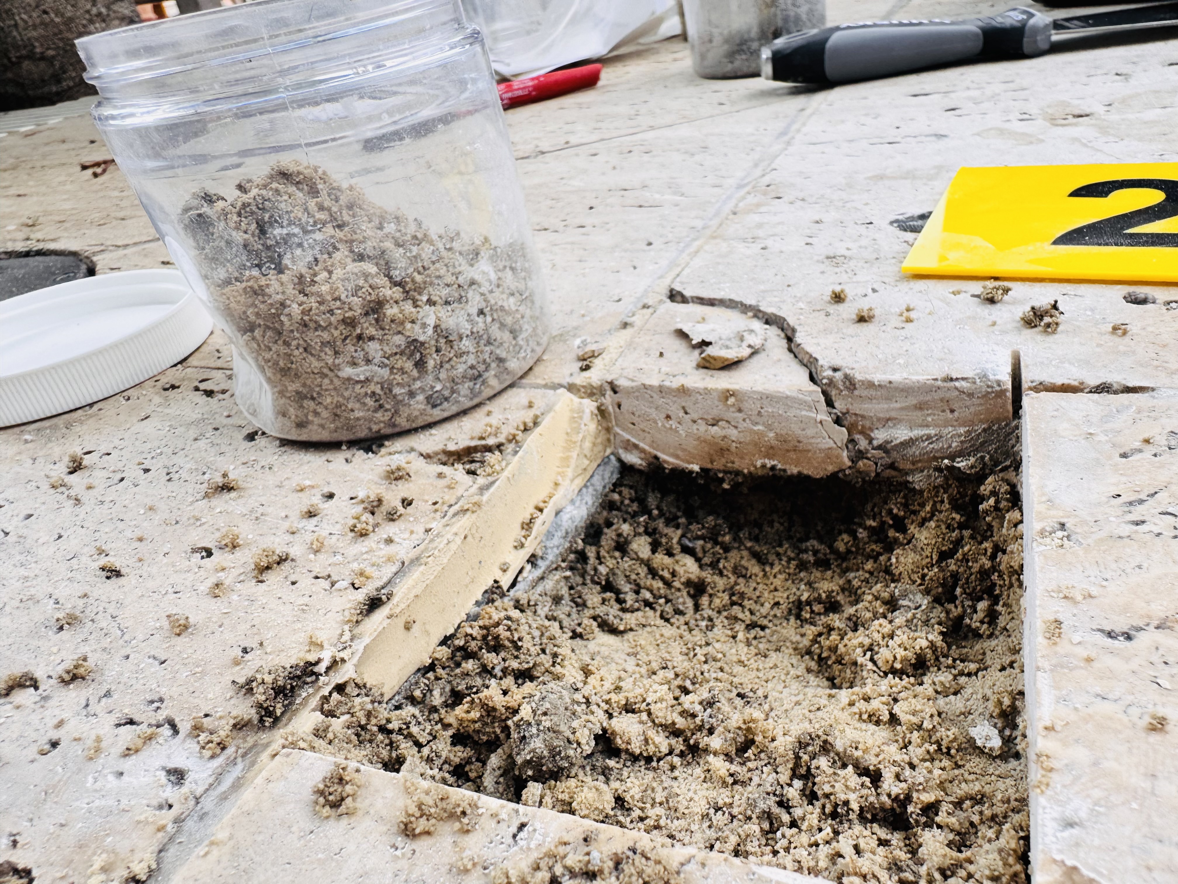 Failed travertine pool deck tile removed exposing oversanded Miami Sandwich mortar bed with collected sample jar