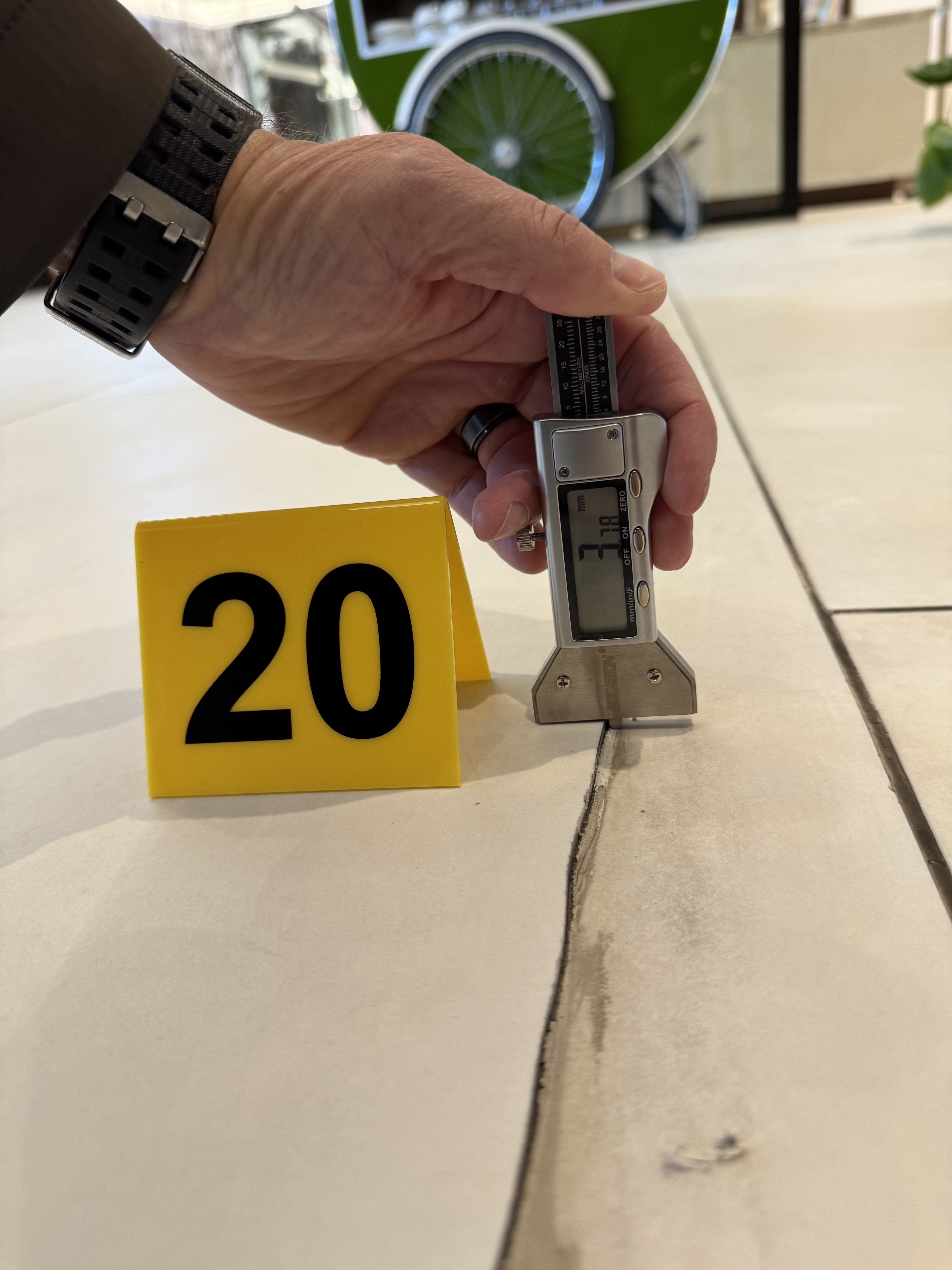 Hand-held digital caliper measuring tile crack at evidence marker 20 in luxury hotel lobby floor