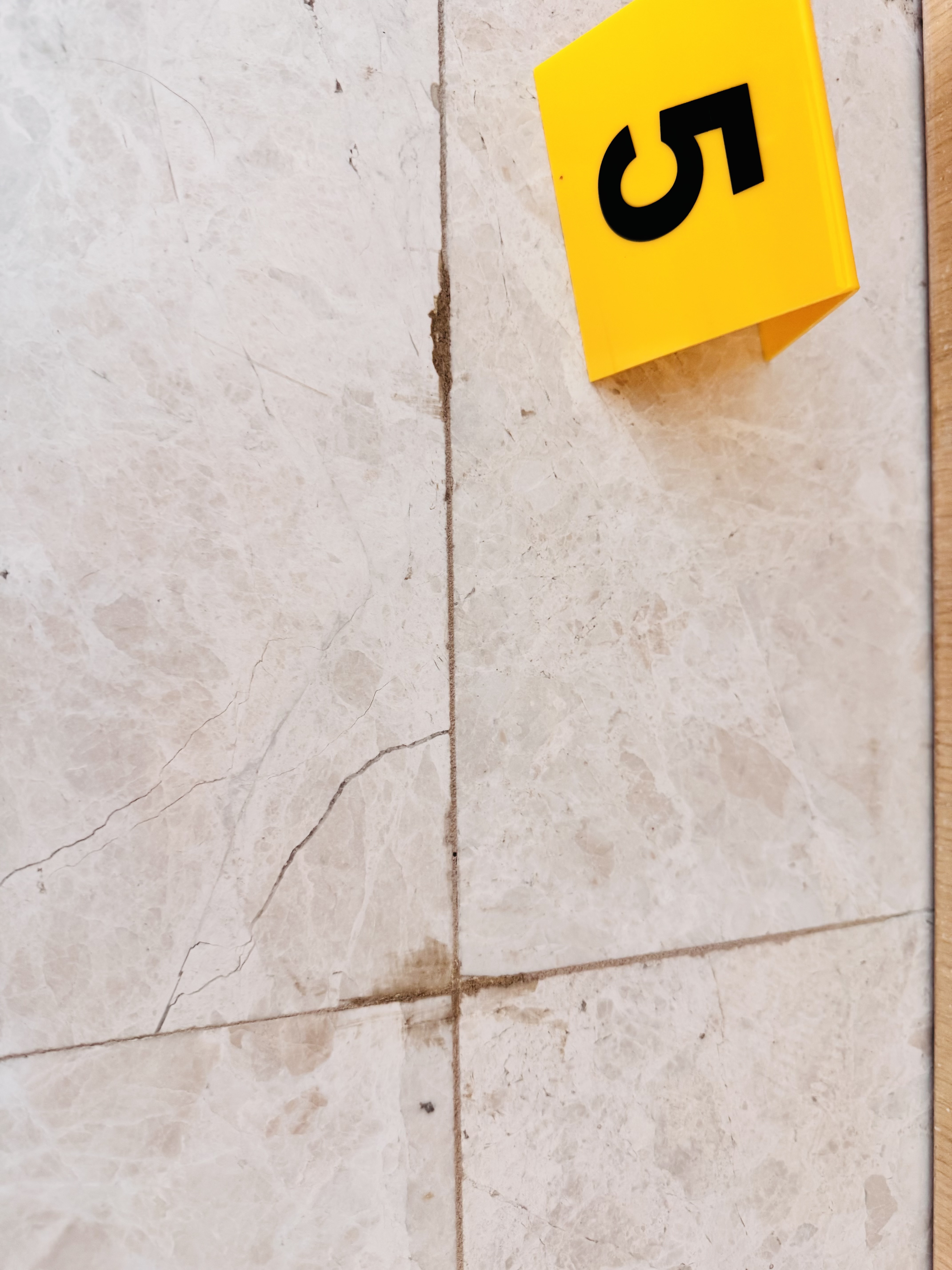 Cracked stone tile at grout joint with forensic evidence marker number 5 showing inadequate joint spacing in luxury residence