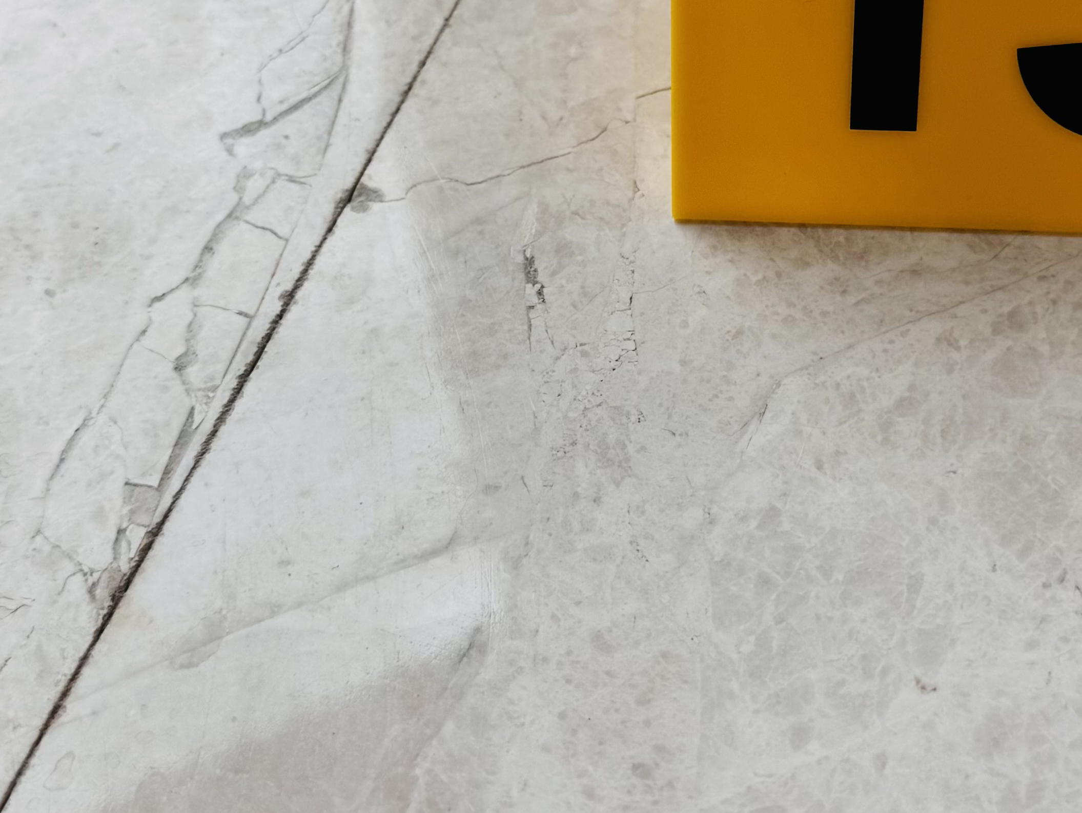 Cracked natural stone tile in luxury home floor with forensic evidence marker documenting failure location