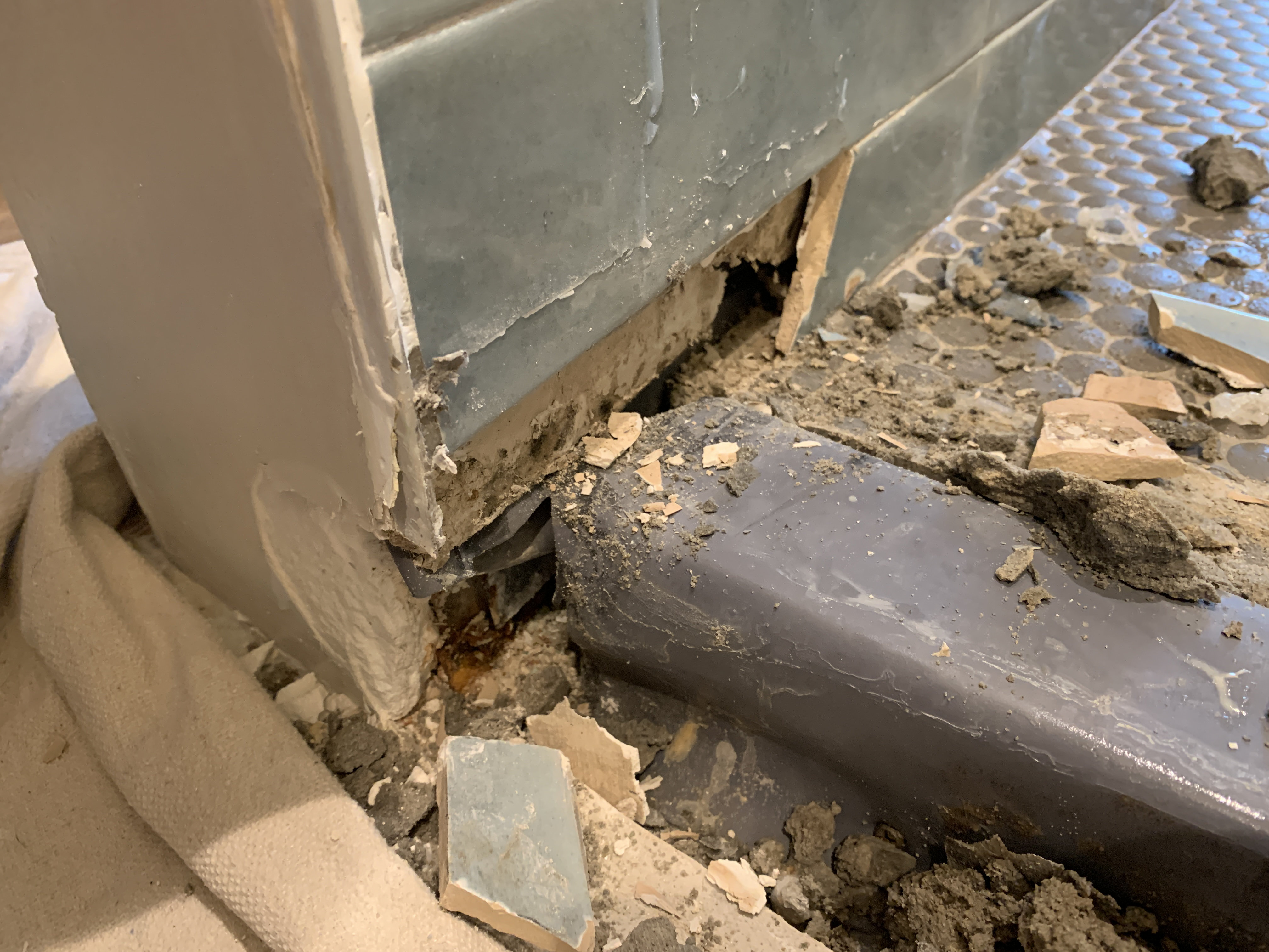 Cut shower liner waterproofing membrane exposed at floor-to-wall transition in hotel bathroom during forensic investigation